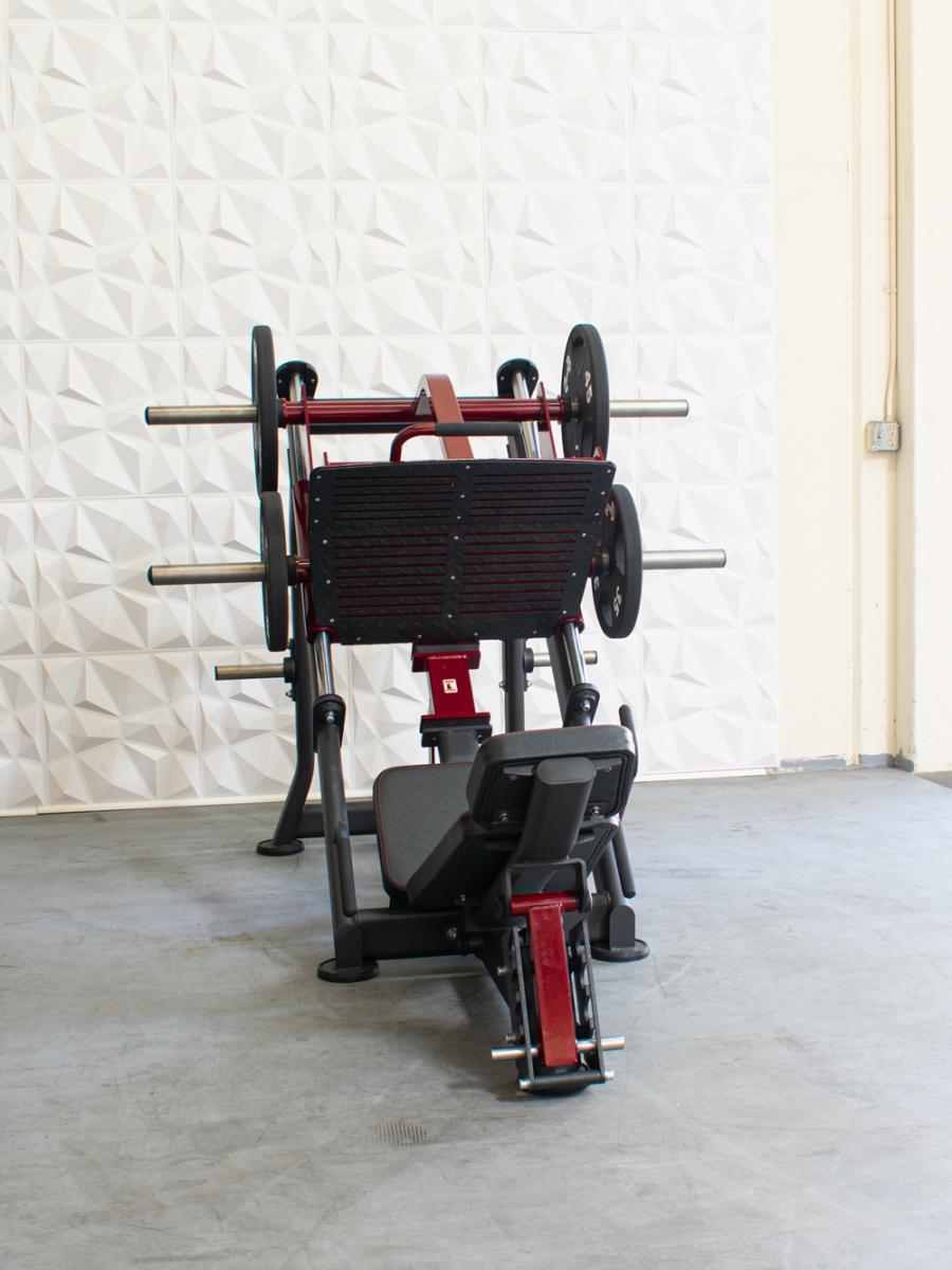 Red and black leg press machine in a gym with a geometric patterned wall.