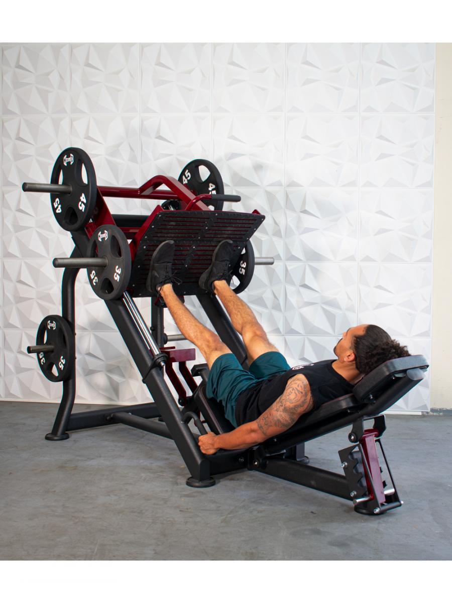 Person using leg press machine with weight plates in gym.