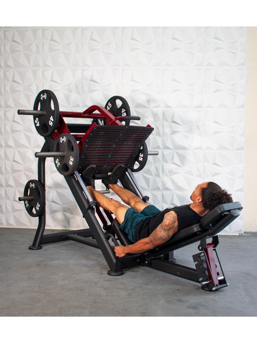 Man using a leg press machine with weight plates in gym.