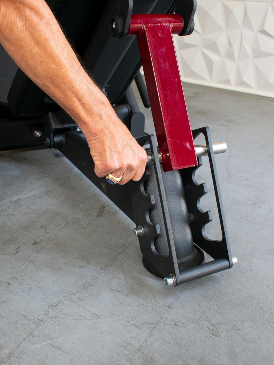 Close-up of a hand adjusting a red-framed leg press machine.