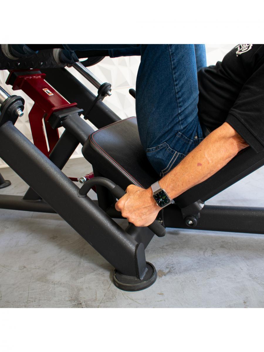 Person using leg press machine, gripping handles, wearing jeans and a watch.