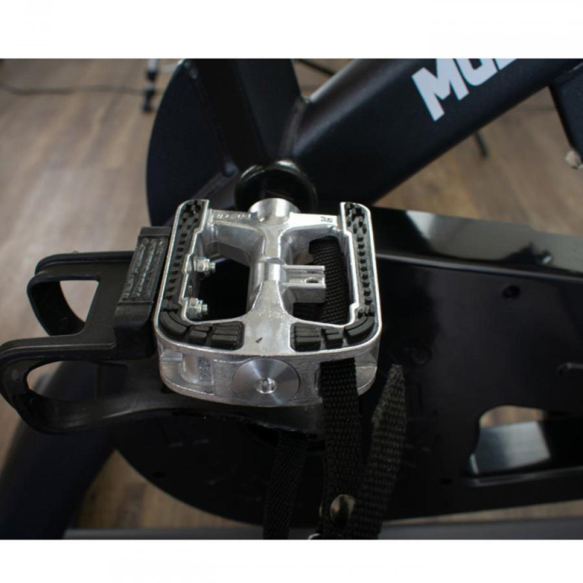 Close-up of metal spin bike pedal with strap and toe cage.