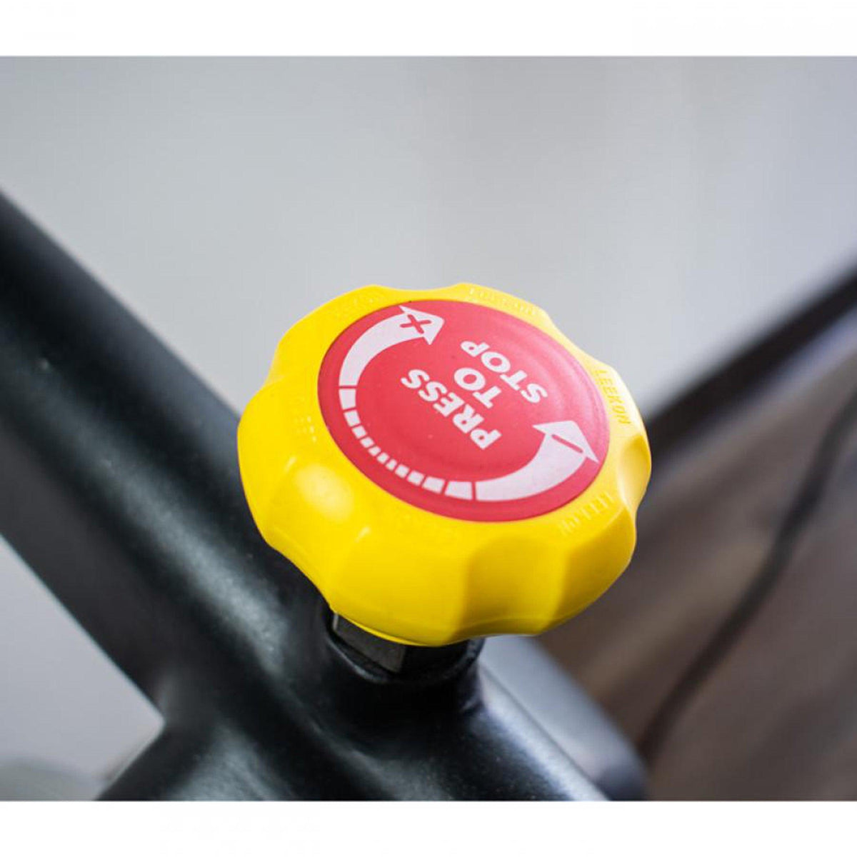 Bright yellow spin-bike adjustment knob with red "Press to stop" label.