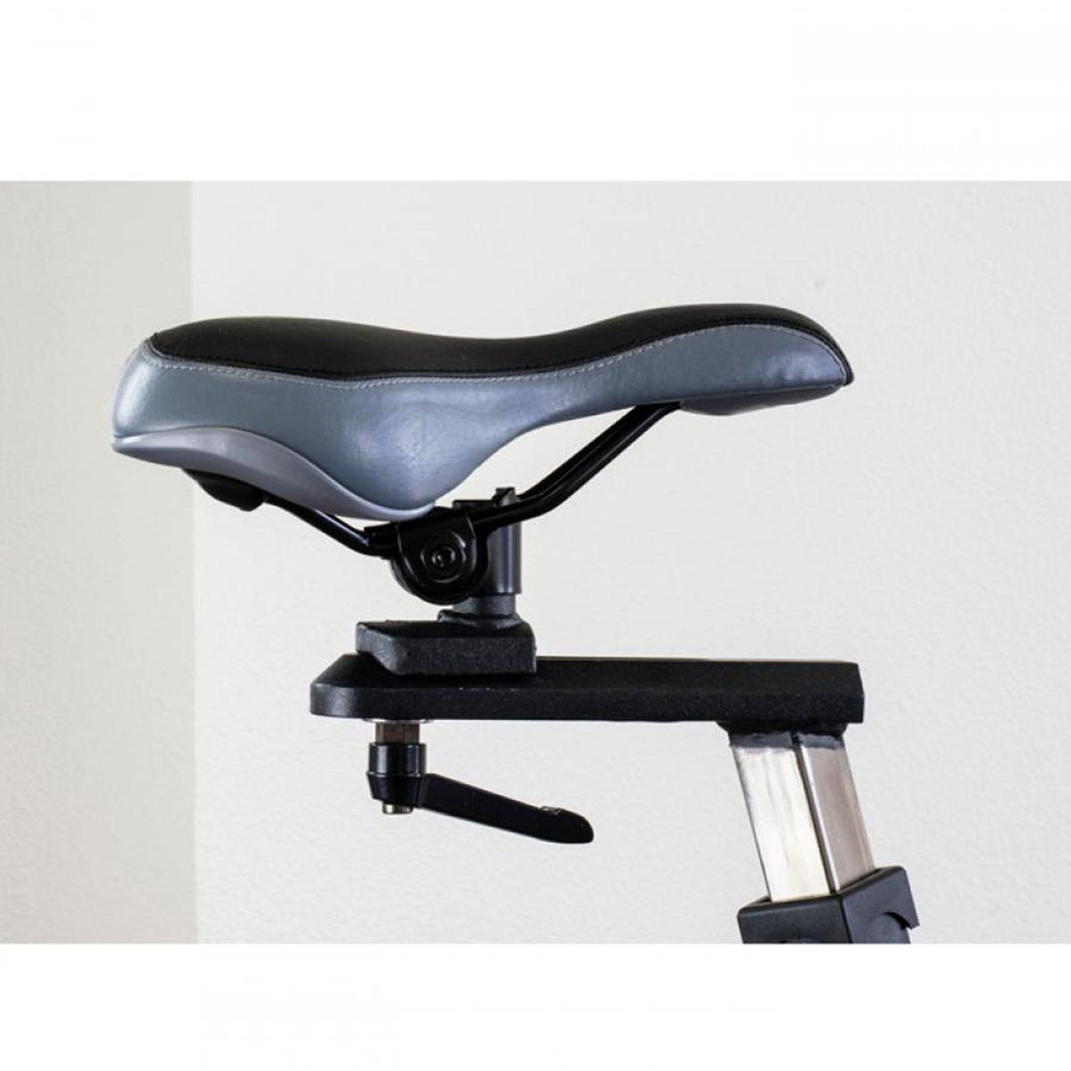 Close-up of a padded bicycle seat on a gym spin bike with adjustable stem.
