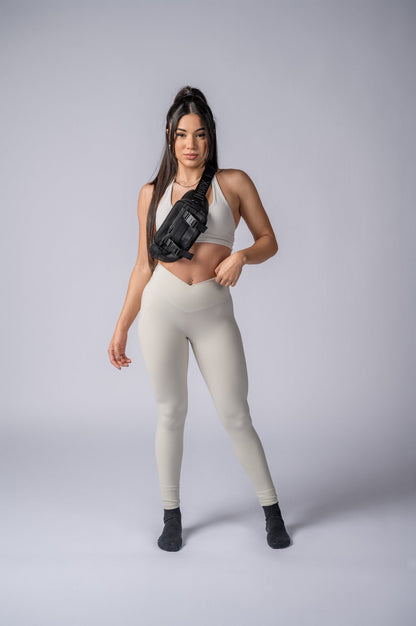 Athletic woman in beige leggings and sports bra with black chest bag.