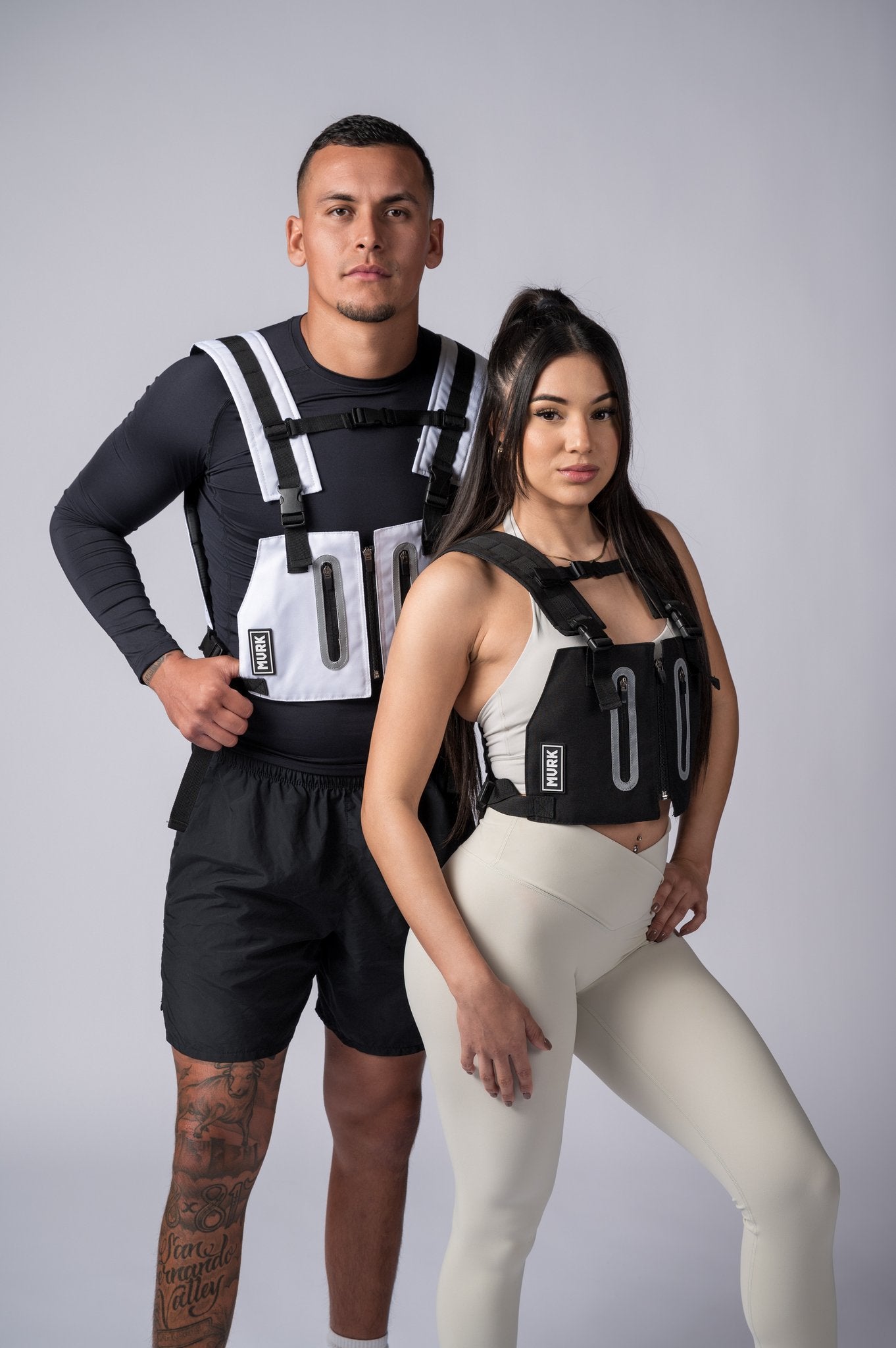 Athletic couple wearing black and white weighted vests posing in studio.