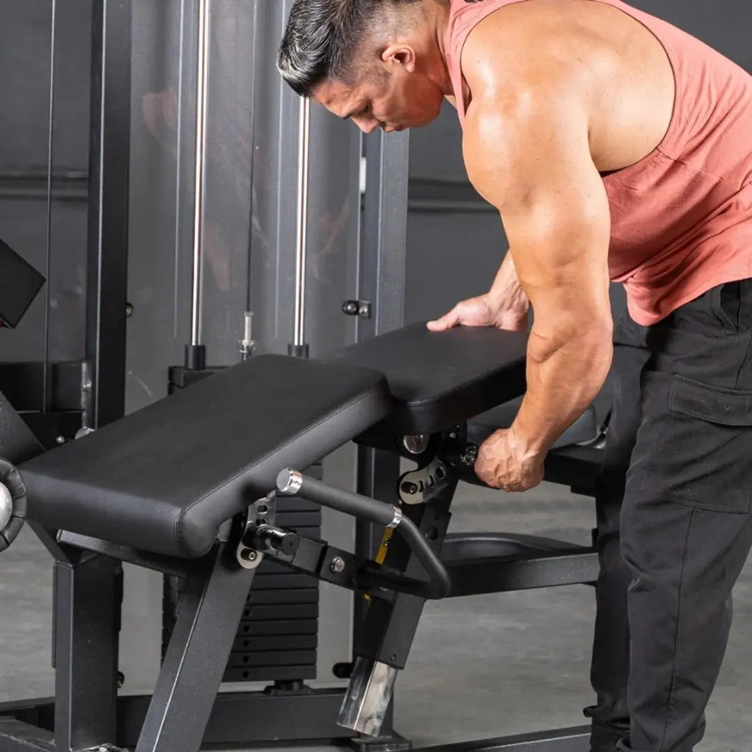 Man performing a leg curl on a black commercial leg curl machine with padded seat and metal frame in a gym setting.