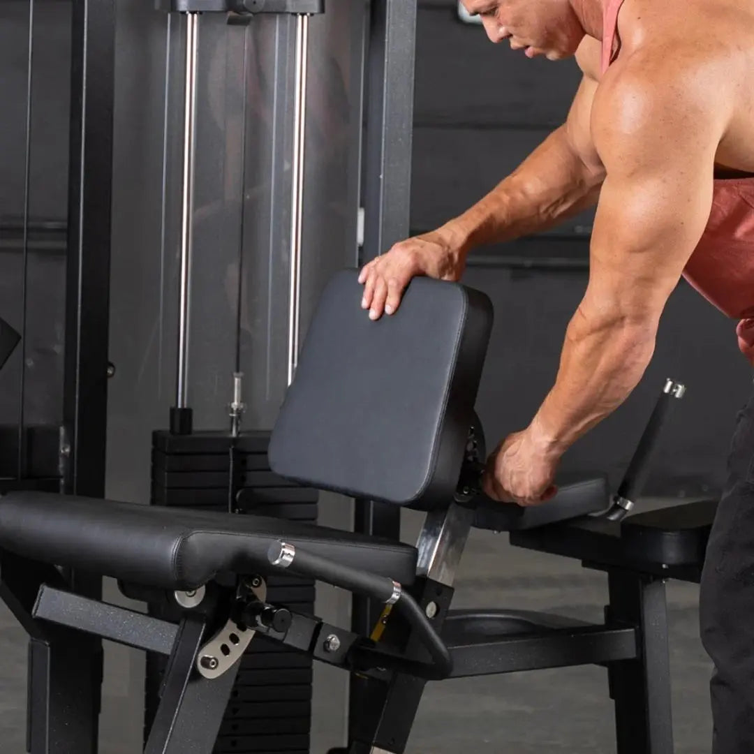 Man performing a leg curl on a black and gray commercial leg curl machine with padded seat and footrest in a gym setting.