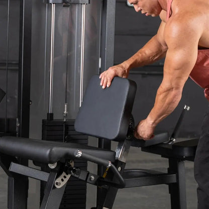 Man performing a leg curl on a black and gray commercial leg curl machine with padded seat and footrest in a gym setting.