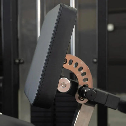 Close-up of a leg extension and lying leg curl combo machine showing the padded black seat back, copper-colored weight plate selector with numbered holes, and adjustment mechanisms in a gym setting.