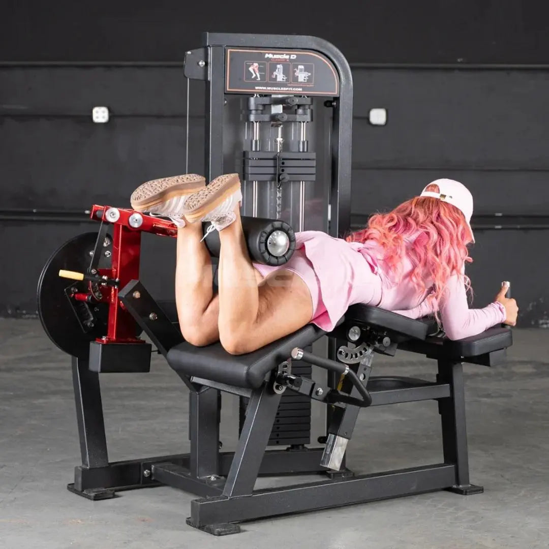 Woman performing lying leg curl on a black and red commercial leg curl machine with digital display panel in a gym setting.