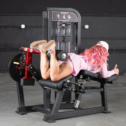 Woman performing lying leg curl on a black and red commercial leg curl machine with digital display panel in a gym setting.