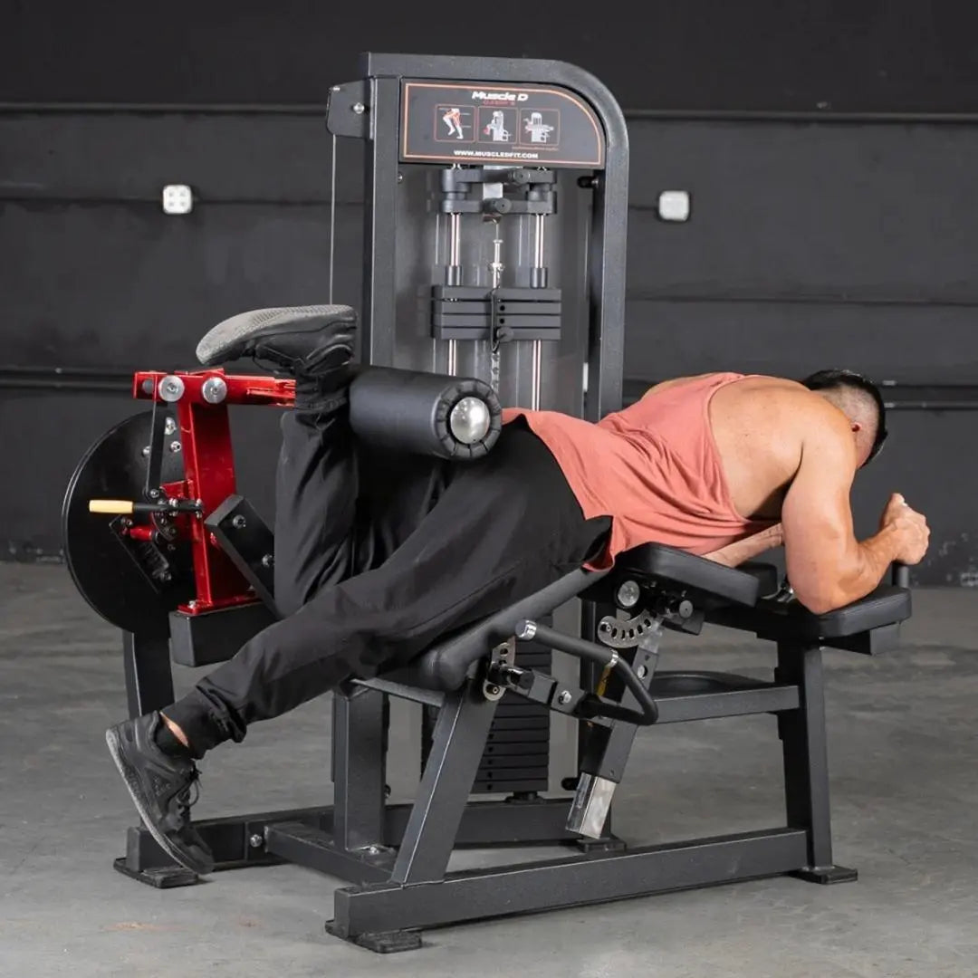 Man performing lying leg curl on a black and red Muscle D Fitness leg extension and leg curl combo machine in a gym setting.