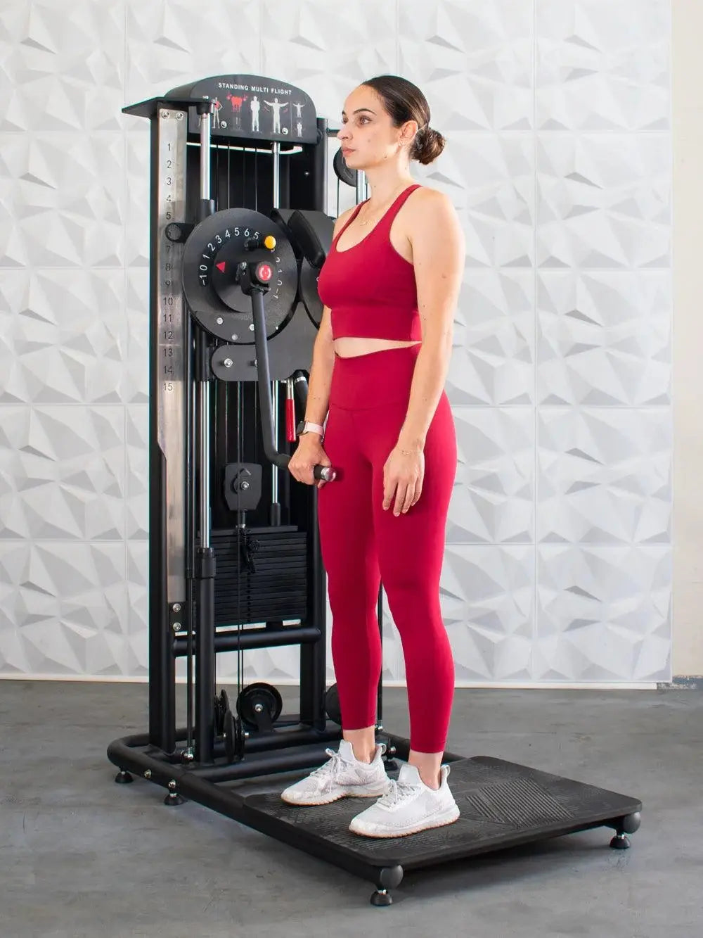 Woman in red workout attire using a black standing multi-flight machine with weight plate selector and exercise position guides on the backrest.