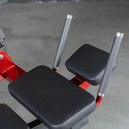 Red and black selectorized abdominal crunch machine with padded seat and back support, gray upright handles, and red frame details on gray studio background.
