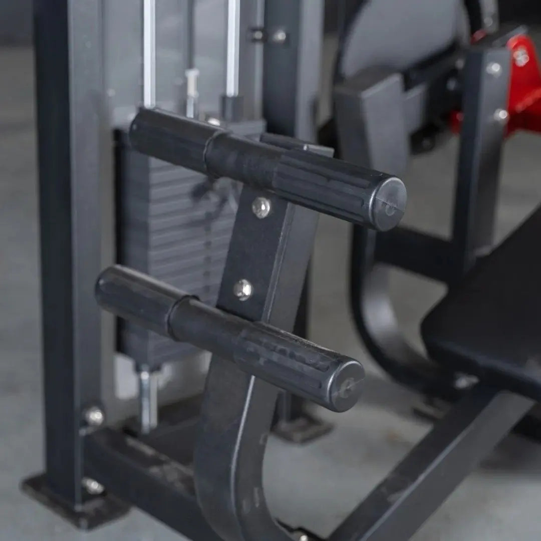 Close-up of black cylindrical handles on a selectorized abdominal crunch machine with metal frame and adjustment mechanisms visible in a gym setting.
