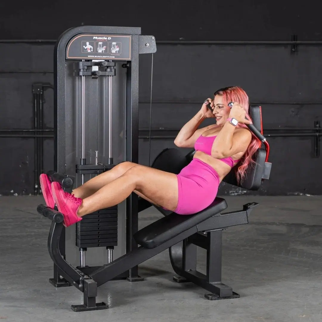 Woman performing an abdominal crunch exercise on a black Muscle D selectorized ab machine with foot platform and weight stack in a gym setting.