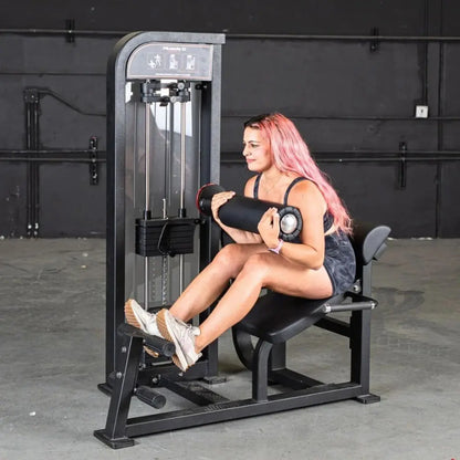 Woman performing a leg extension exercise on a black selectorized back and ab combo machine in a gym setting.