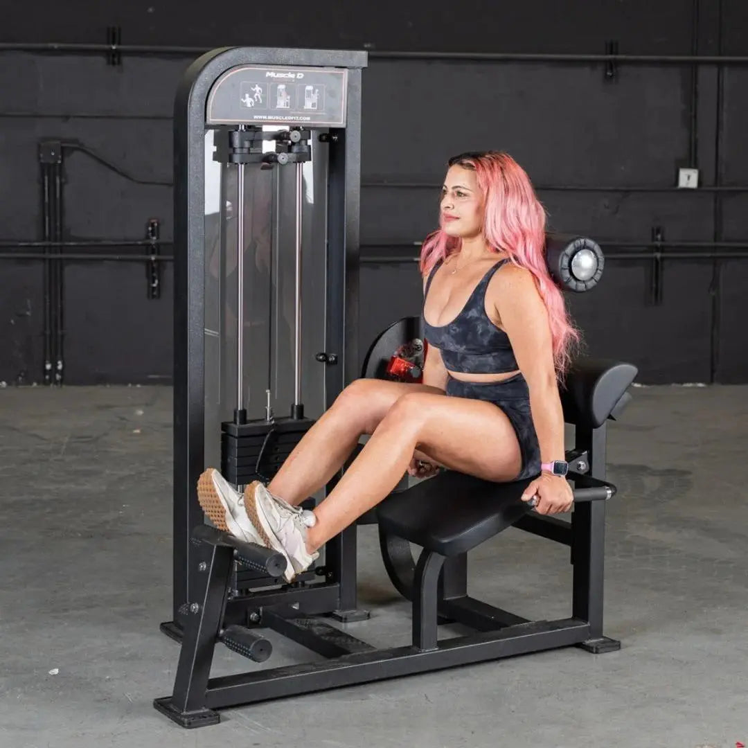 Woman performing leg extension on a black selectorized back and ab combo machine in a gym with dark walls.