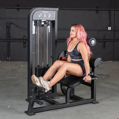 Woman performing leg extension on a black selectorized back and ab combo machine in a gym with dark walls.