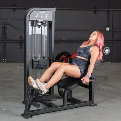 Woman performing a leg extension exercise on a black selectorized leg extension and ab machine in a gym with dark walls.