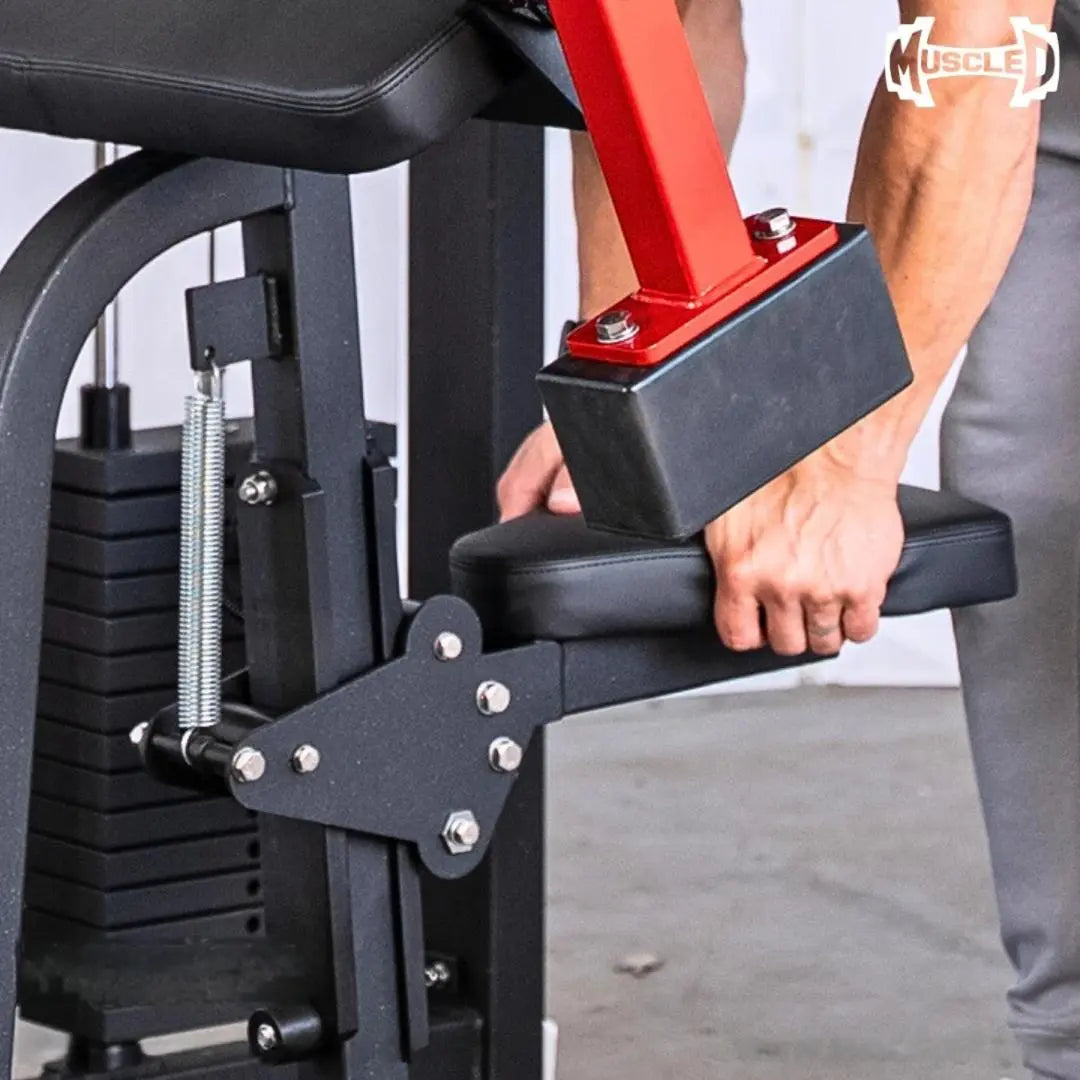 Man performing a biceps curl on a black and red selectorized gym machine with a padded arm rest and weight stack visible on the left side.