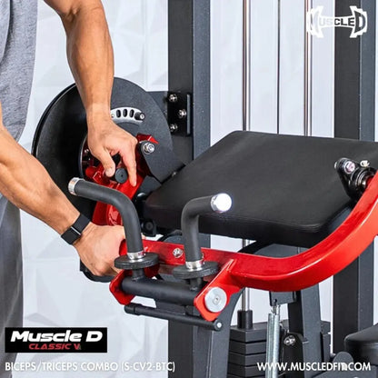 Man performing biceps curl on a Muscle D Classic V2 selectorized biceps and triceps combo machine with red frame, black padded seat, and weight stack visible in background.