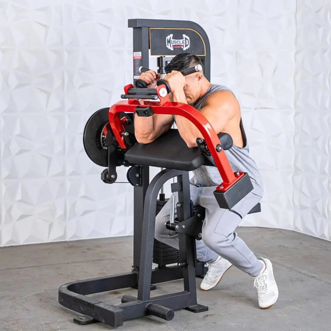 Man performing a biceps and triceps exercise on a red and black selectorized cable machine with black seat and foot platform.