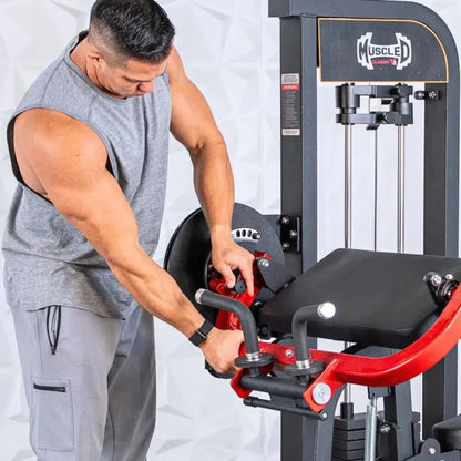 Man performing a biceps curl on a Muscle D Fitness selectorized cable machine with red and black frame and black padded seat.