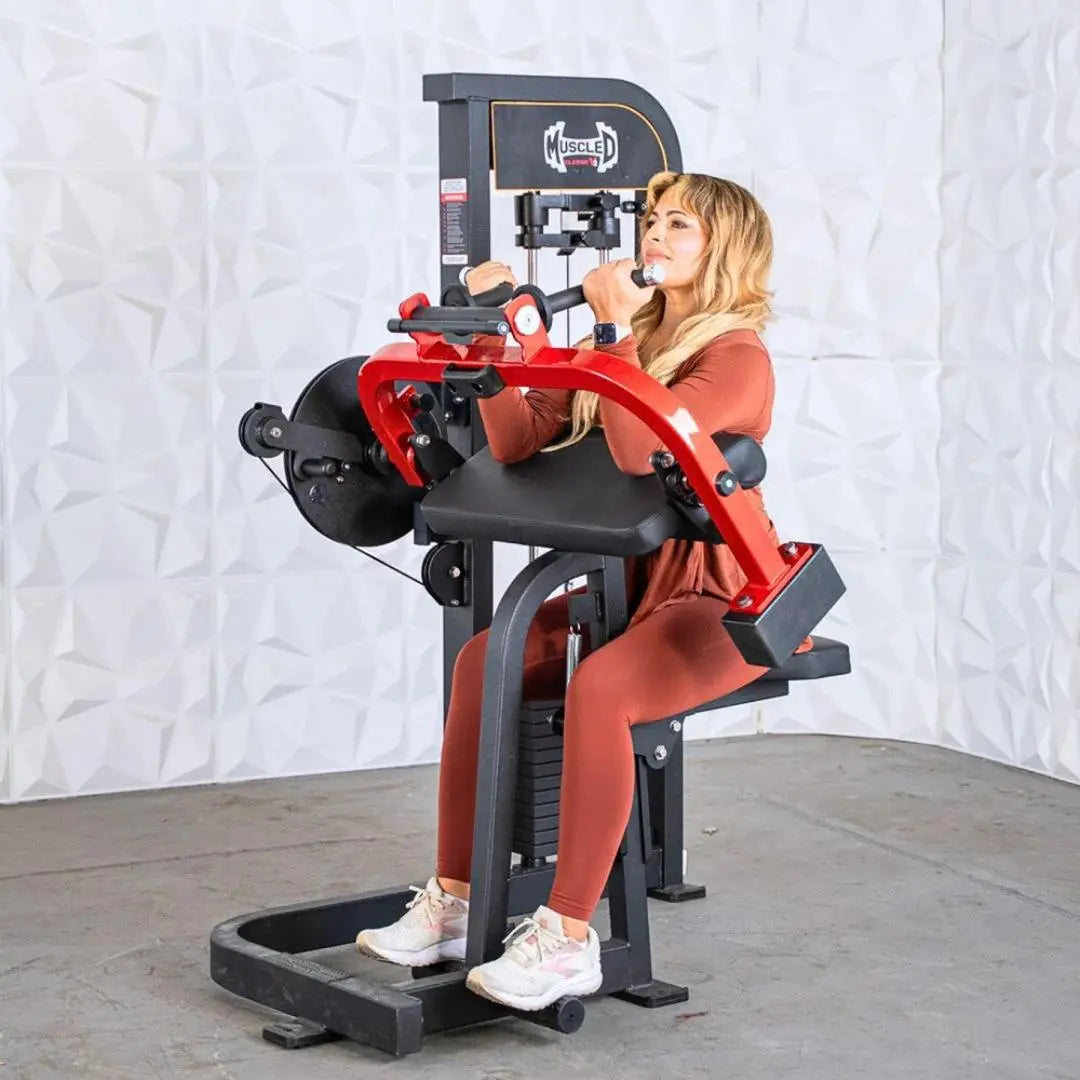 Woman performing a biceps and triceps curl on a red and black Muscle D Fitness selectorized combo machine with dark gray upholstery and black foot platform.