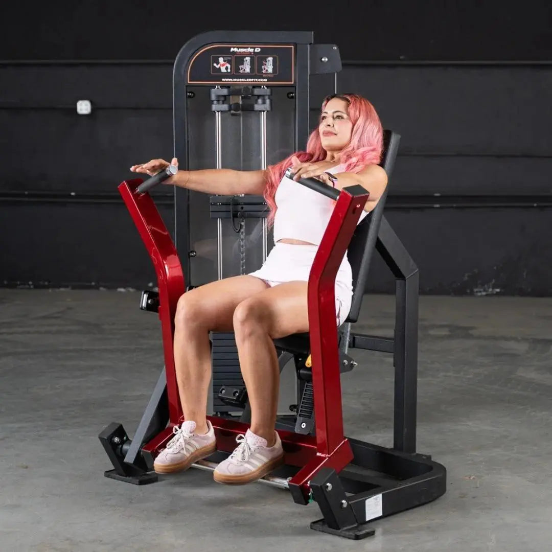 Woman performing a chest press exercise on a red and black selectorized chest press machine with dual handles in a gym setting.