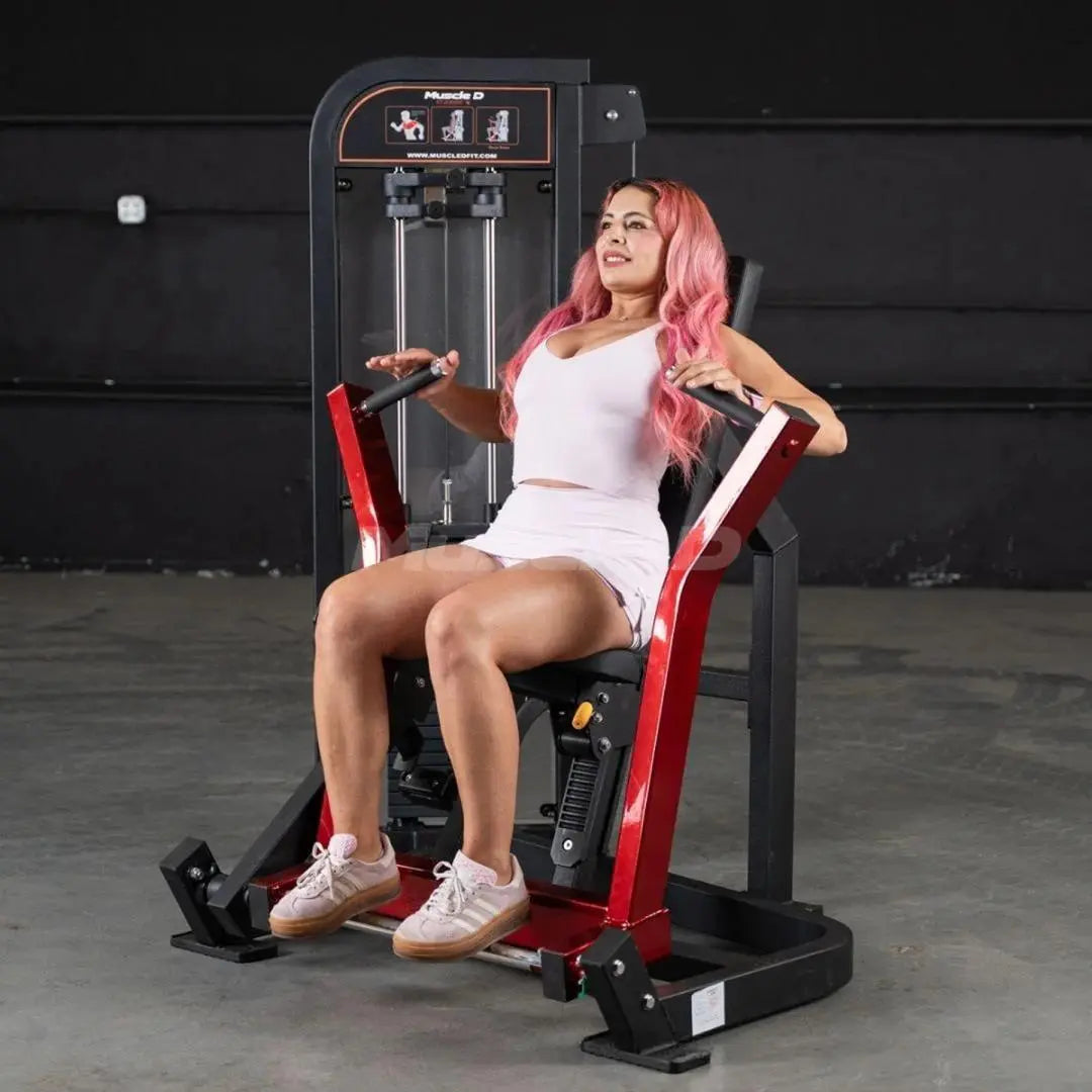 Woman performing chest press on a Muscle D Fitness selectorized machine with red and black frame in a gym setting.