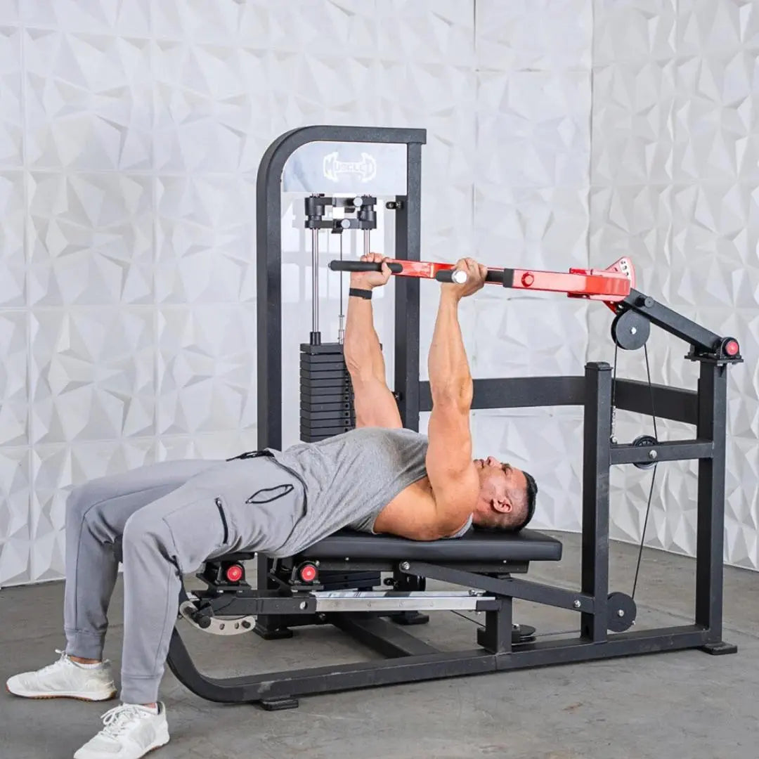 Man performing a chest press exercise on a black and red selectorized machine with weight stack and adjustable arm lever against a white textured wall.