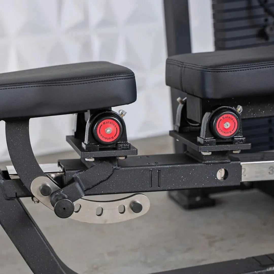 Close-up of the seat and foot pedal mechanism on a selectorized chest and shoulder machine, showing black padded seat, red resistance knobs, and adjustable pedal assembly with metal components.