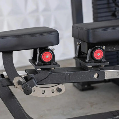 Close-up of the seat and foot pedal mechanism on a selectorized chest and shoulder machine, showing black padded seat, red resistance knobs, and adjustable pedal assembly with metal components.