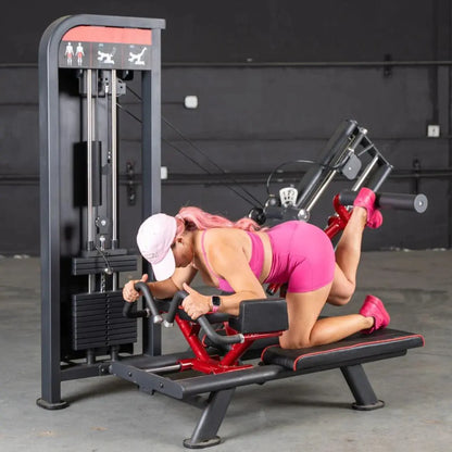 Woman performing a glute kick exercise on a red and black selectorized machine with gray frame and instruction icons displayed on the top panel.