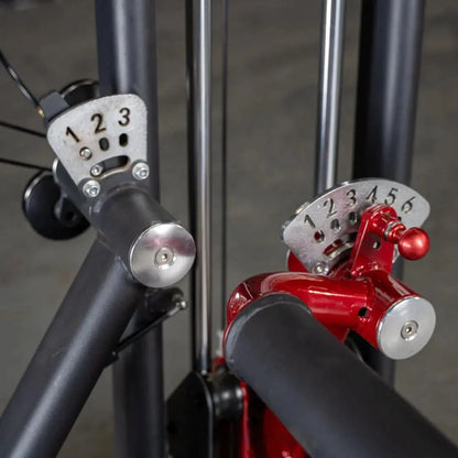Close-up of selector pins on a glute kick machine, showing numbered weight increments on white and red adjustment plates mounted on black and red machine arms.