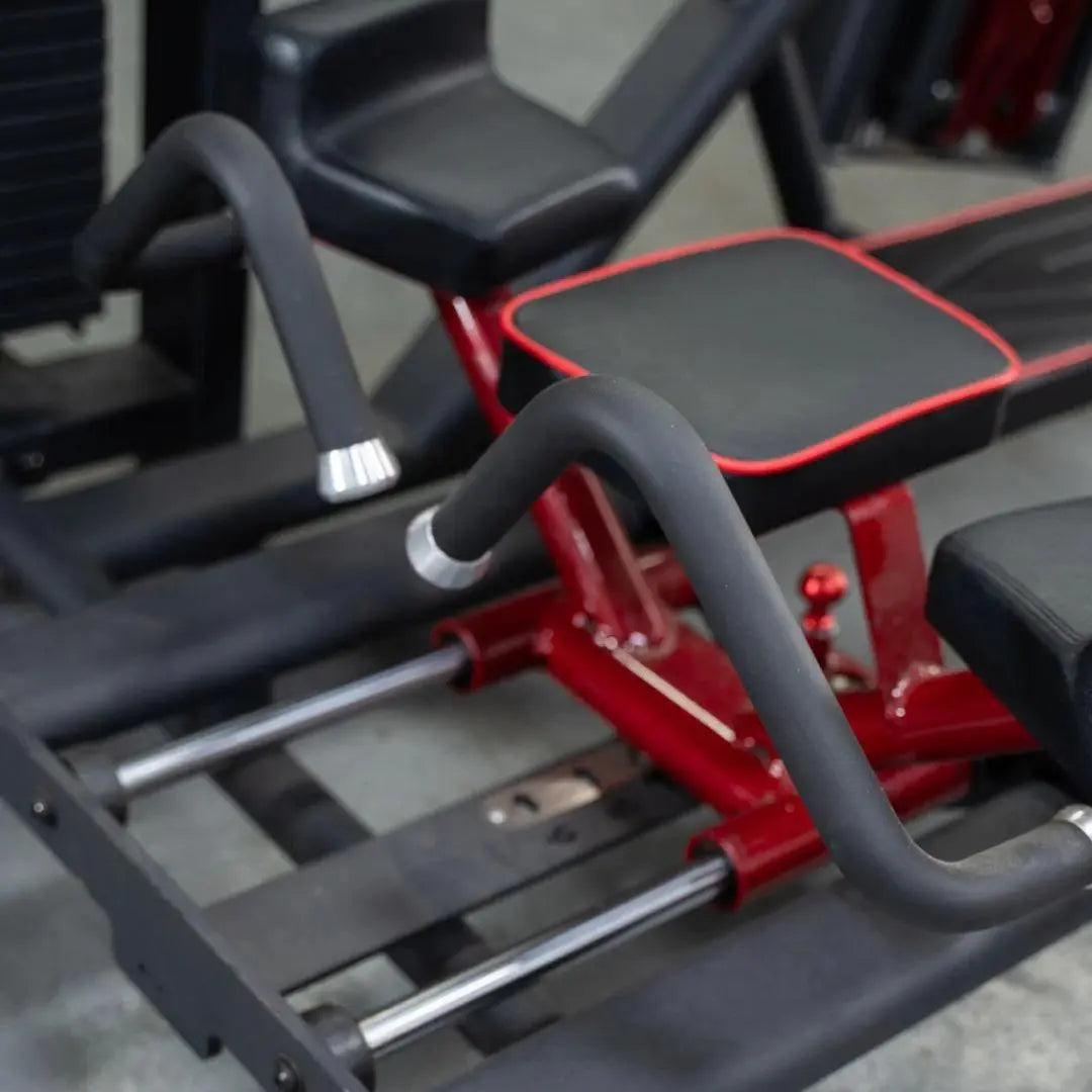 Selectorized glute kick machine with red metal frame, black padded seat and backrest, and gray foam-covered handles. Multiple weight plate pegs visible on the side.
