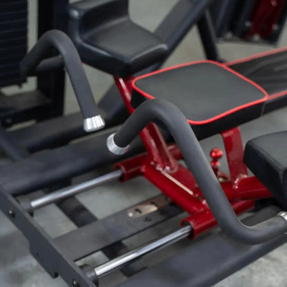 Selectorized glute kick machine with red metal frame, black padded seat and backrest, and gray foam-covered handles. Multiple weight plate pegs visible on the side.