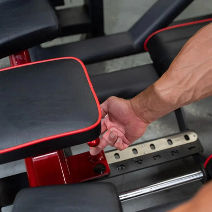 Man's hand gripping the red handle of a glute kick machine with black padded seat and adjustment lever visible.