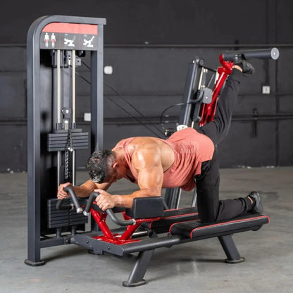 Man performing a glute kick exercise on a red and black selectorized machine with gray frame in a gym setting.