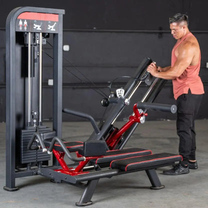 Man performing a glute kick exercise on a black and red selectorized leg press machine with gray frame and instruction icons on the top panel.