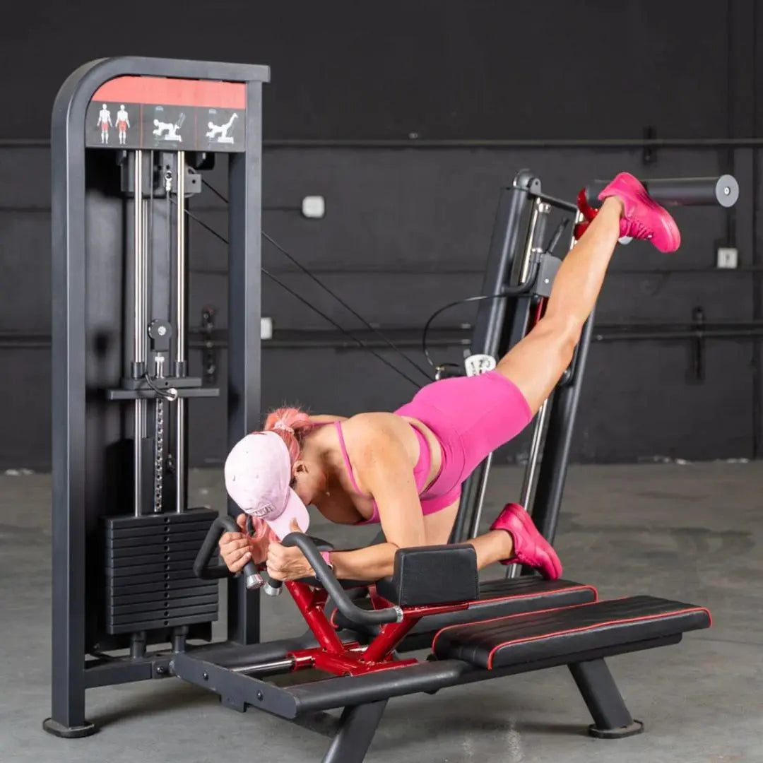 Woman performing leg extension on a commercial glute kick machine with red frame and black upholstery in a gym setting.