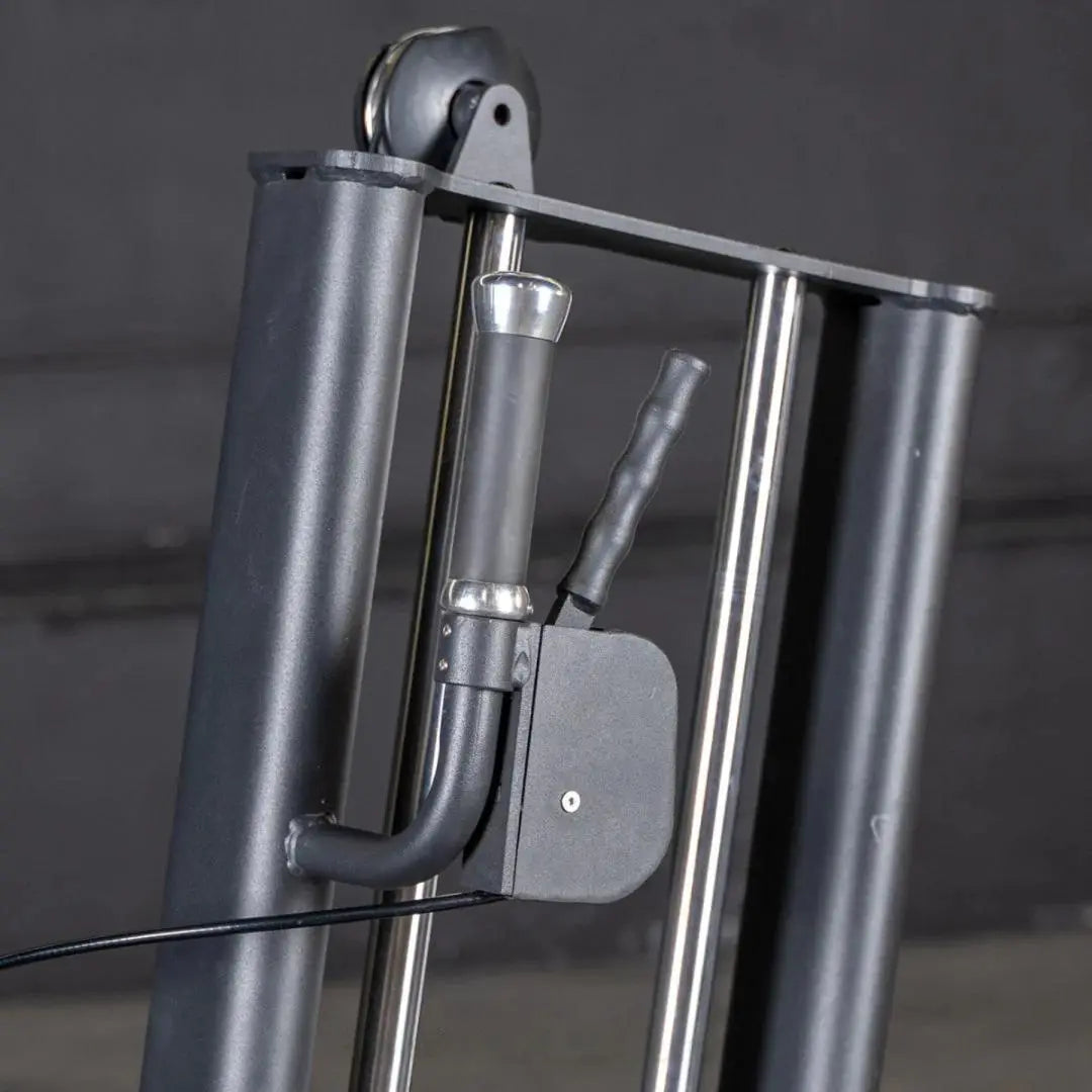 Close-up of a selectorized glute kick machine showing chrome frame with padded footrest, black lever arm, and metal weight stack selector pin on gray studio background.