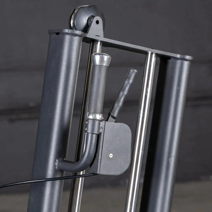 Close-up of a selectorized glute kick machine showing chrome frame with padded footrest, black lever arm, and metal weight stack selector pin on gray studio background.