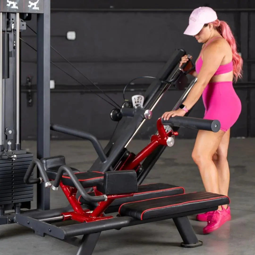 Woman performing a glute kick exercise on a red and black selectorized leg machine with handle bars in a gym setting.