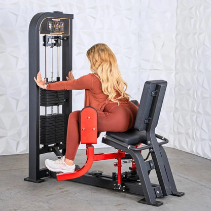 Woman performing inner and outer thigh exercises on a black and red selectorized leg machine with dual work stations in a gym setting.
