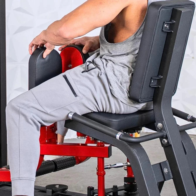 Man performing inner and outer thigh exercise on a selectorized machine with black backrest and red weight stack frame.