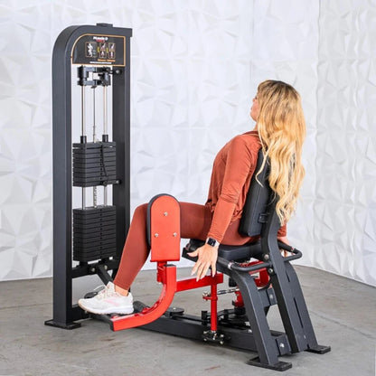 Woman performing inner and outer thigh exercise on a red and black selectorized leg machine with weight stack in a gym setting.