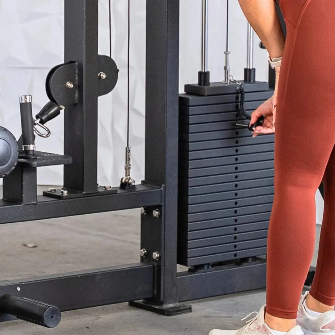 Woman in red leggings adjusting the pin on a black selectorized lat pulldown and low row combo machine with stacked weight plates.